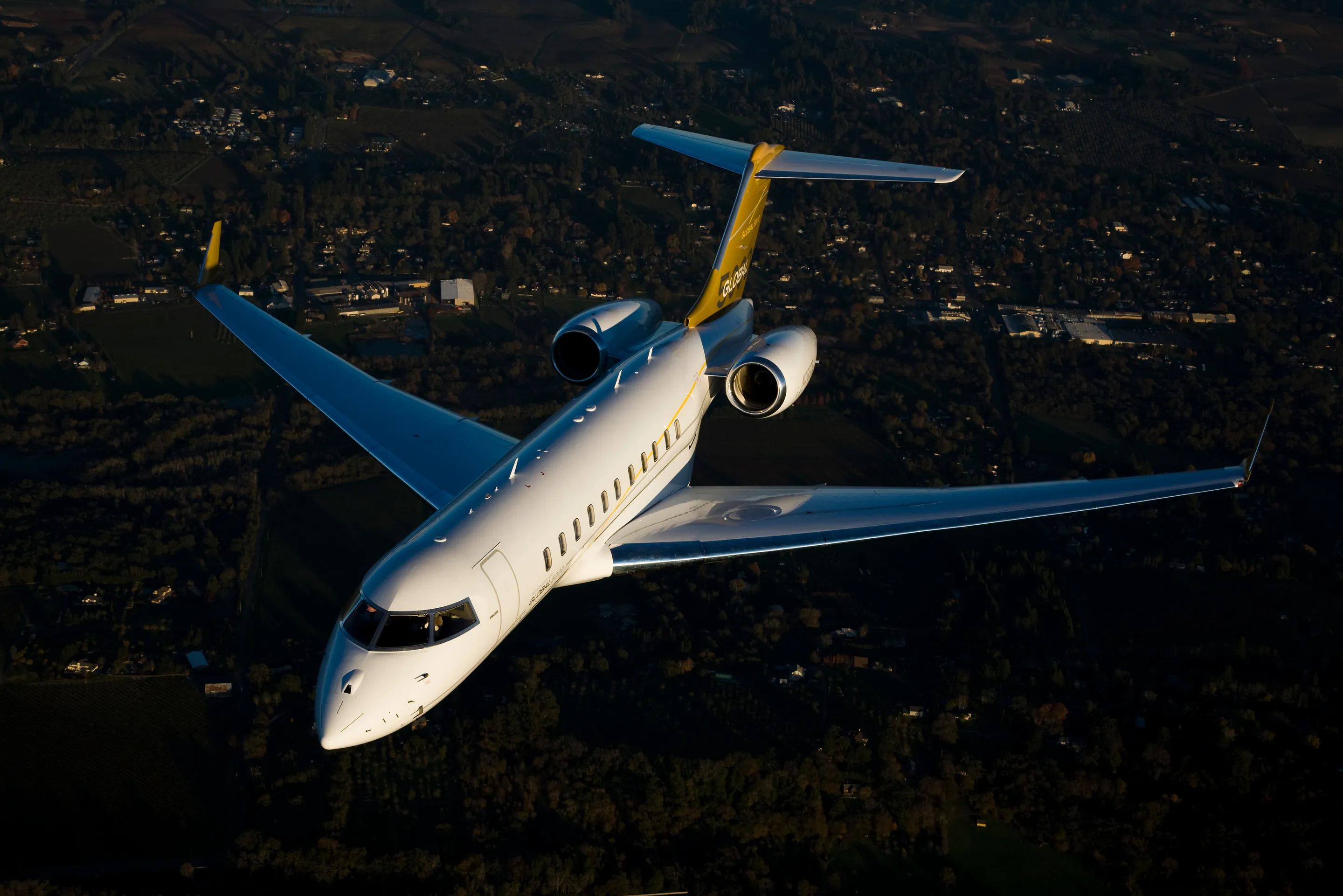 A Bombardier Global seen from above, flying over farmland in the last evening light.