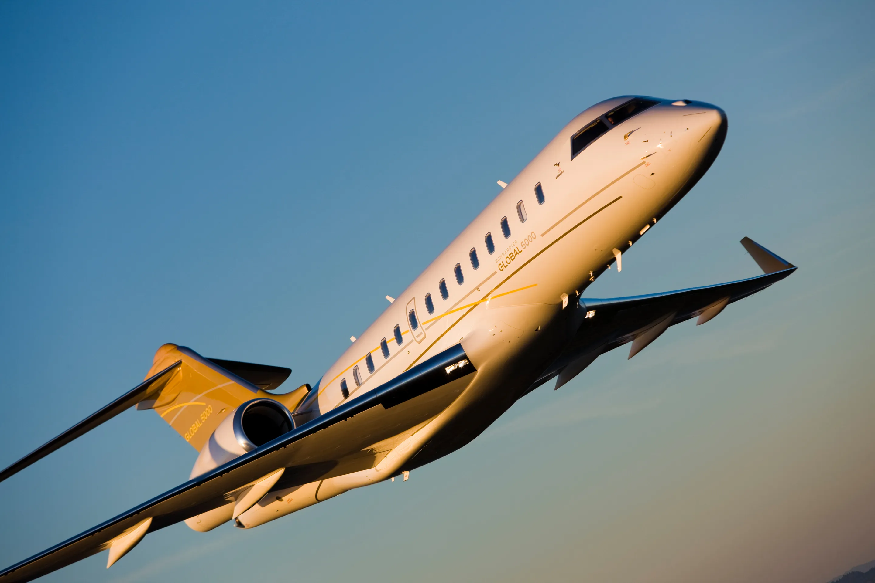 A Bombardier Global 5000 climbing into a clear evening sky.