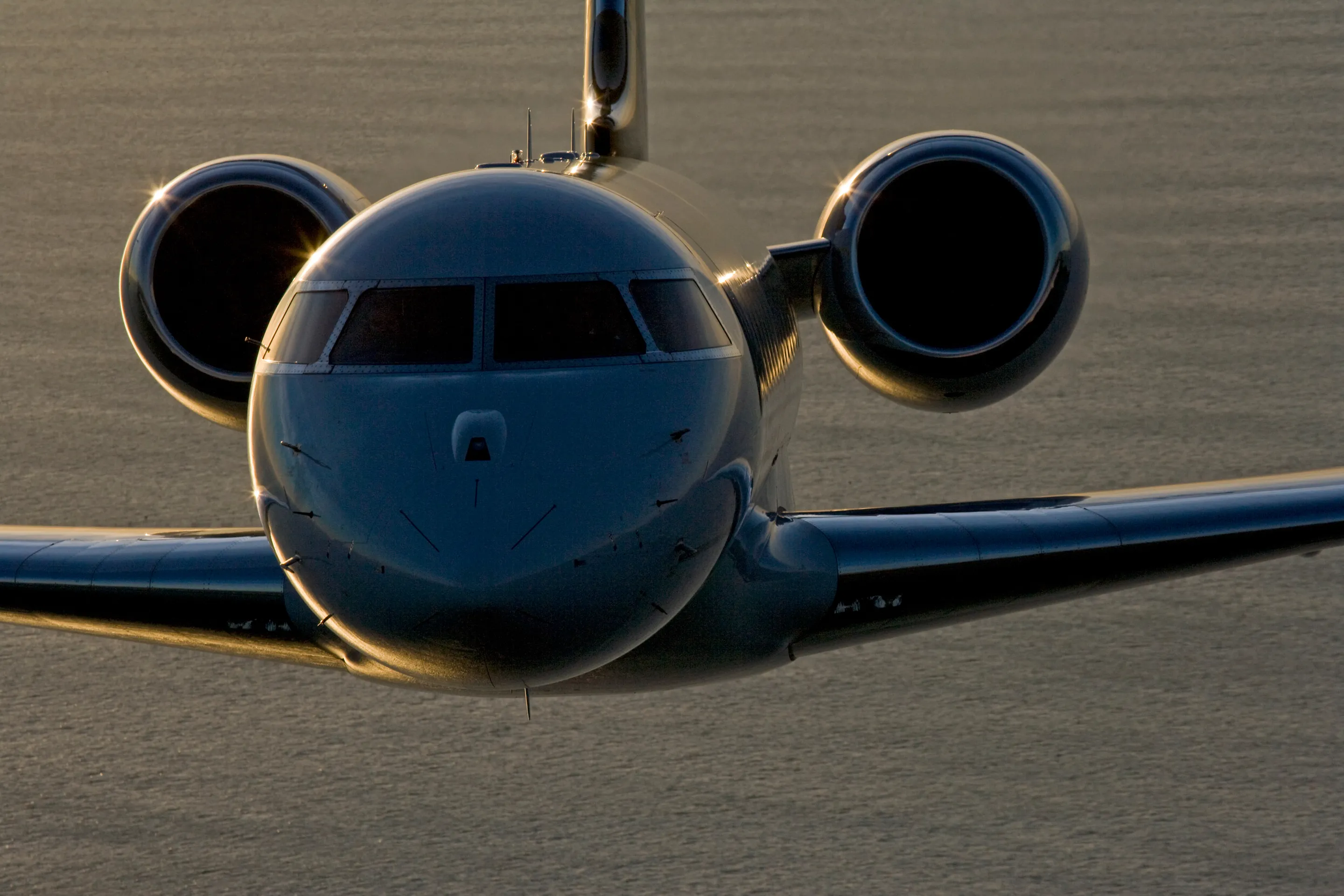 A Bombardier Global seen head-on in flight, its engines catching the low sun.