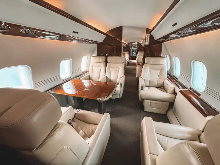 Bombardier Global cabin with club seats and a polished veneer table in warm evening light.