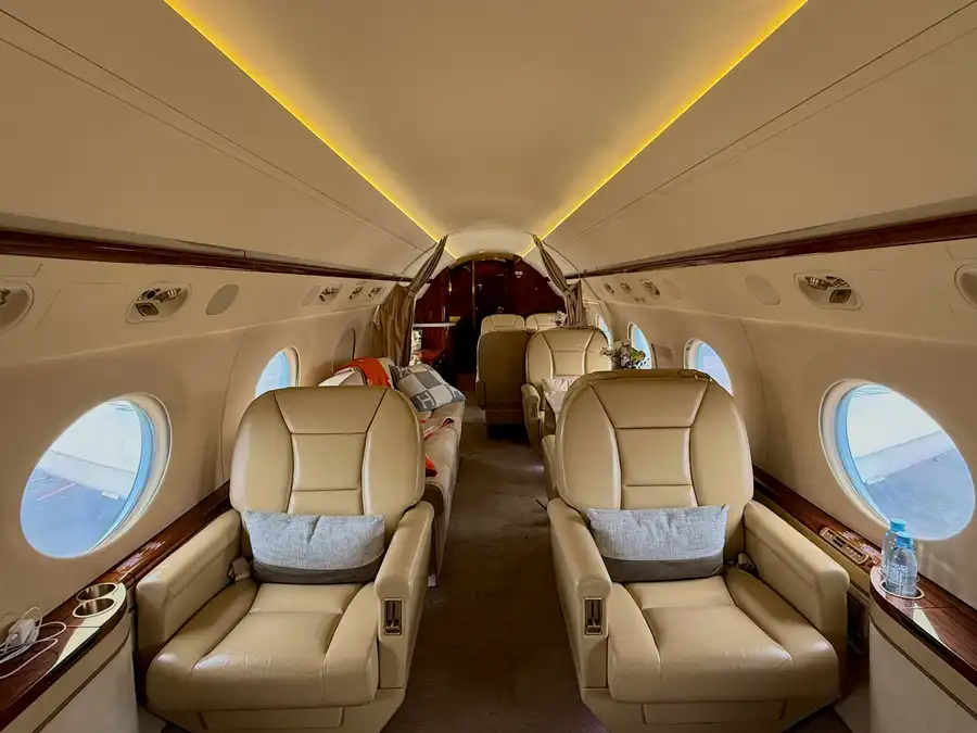 Gulfstream cabin with cream leather seats and wood veneer under warm cove lighting.